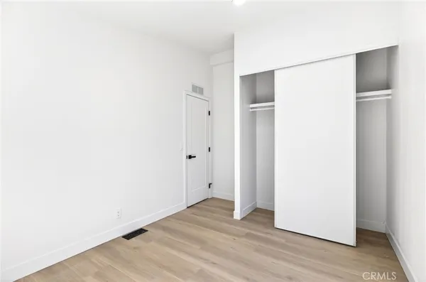 a view of an empty room with wooden floor and closet