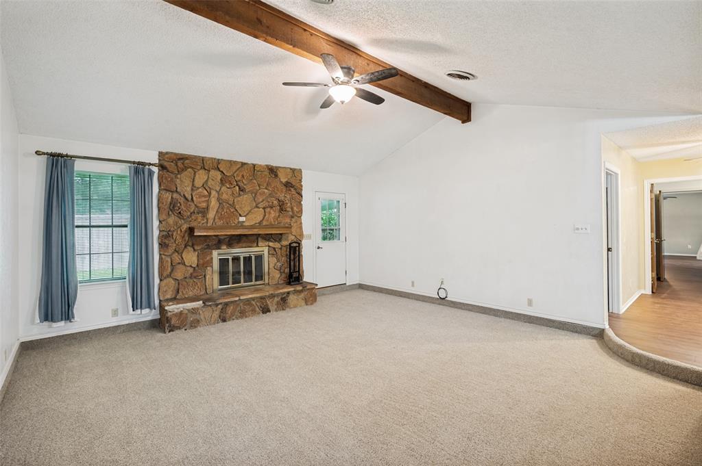 508 South Pedigo Street Pilot Point, TX 76258 - Photo 3 of 26 Spacious living area featuring a stone-clad fireplace with a hearth, vaulted ceiling, exposed wood beam, ceiling fan, and large window