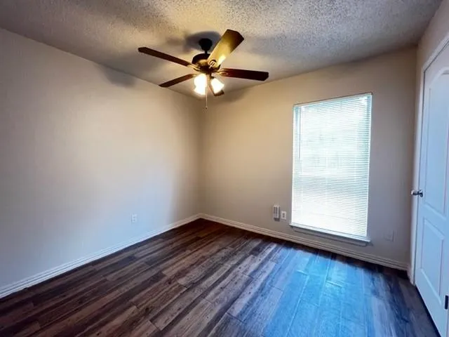 an empty room with wooden floor fan and windows