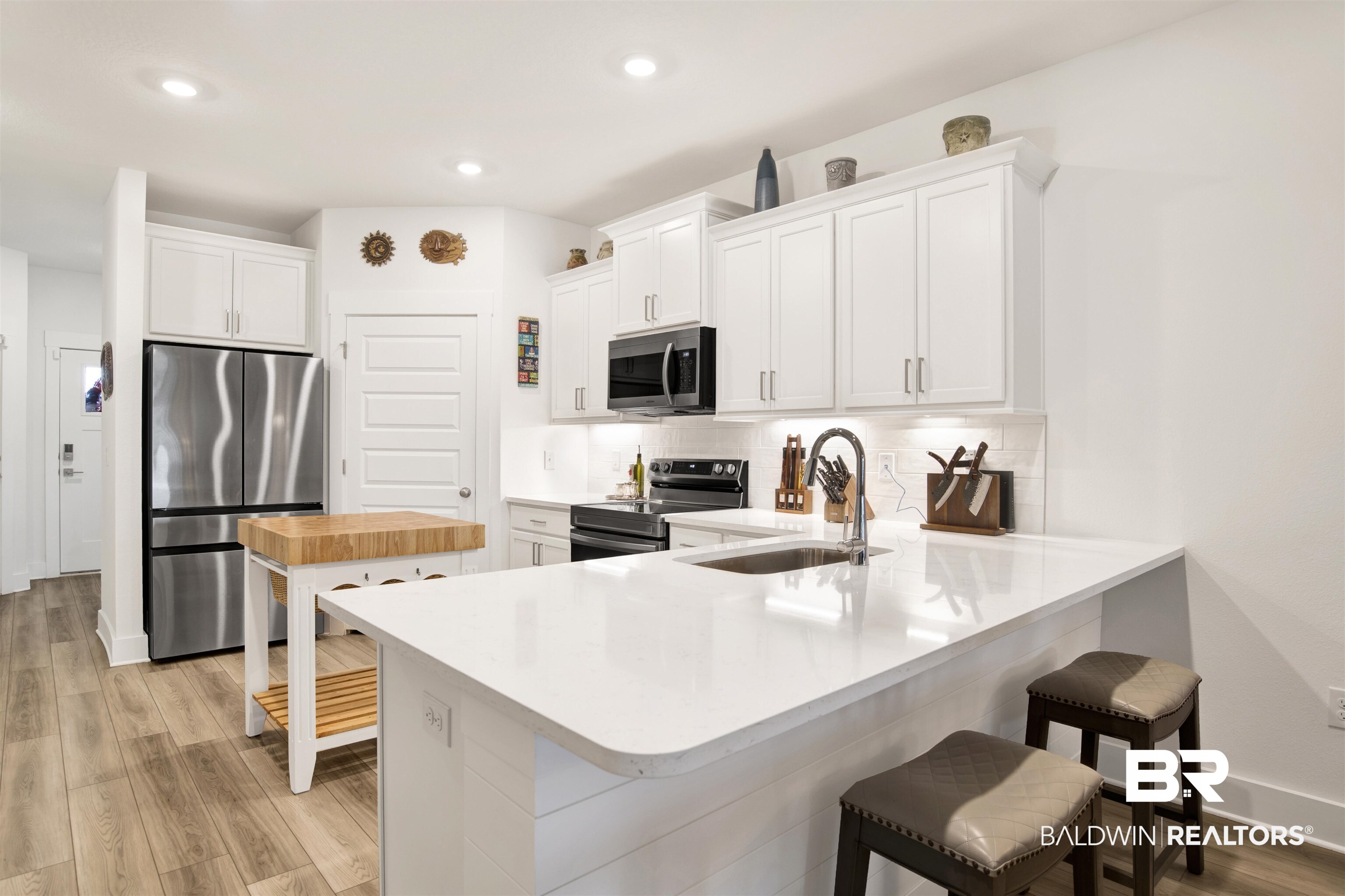 Kitchen with appliances with stainless steel finishes, light wood-type flooring, light countertops, a breakfast bar area, and white cabinetry