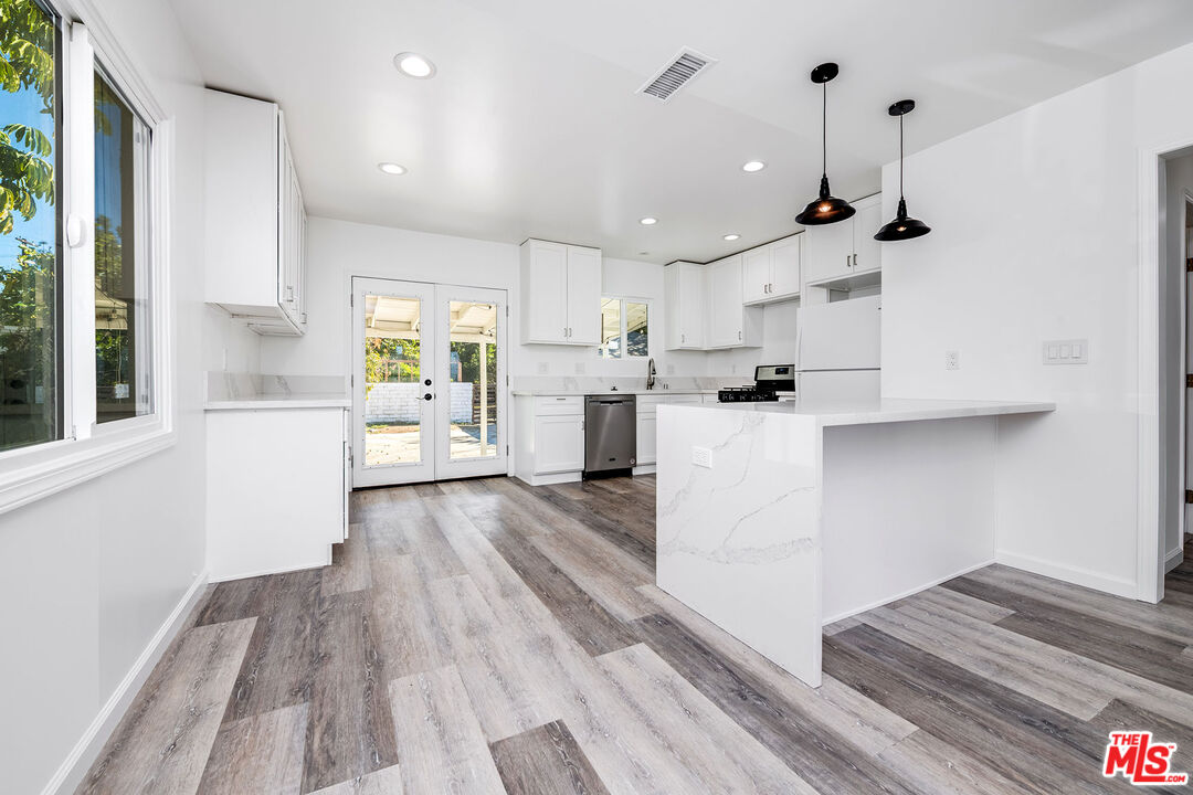 7422 Milwood Avenue Canoga Park, CA 91303 - Photo 5 of 15 a kitchen with stainless steel appliances kitchen island wooden floors and white cabinets