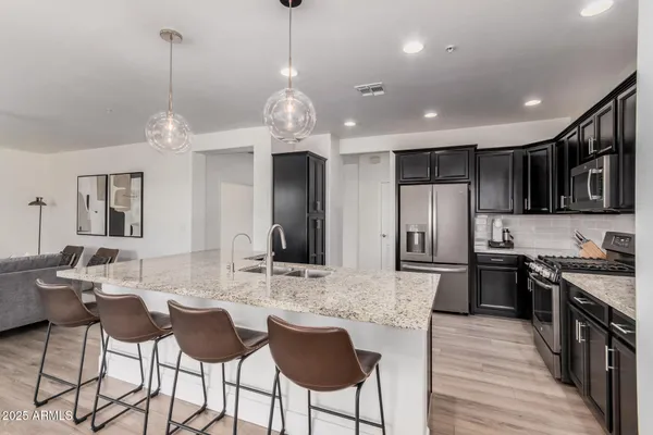 a kitchen with stainless steel appliances kitchen island granite countertop a dining table chairs refrigerator and cabinets