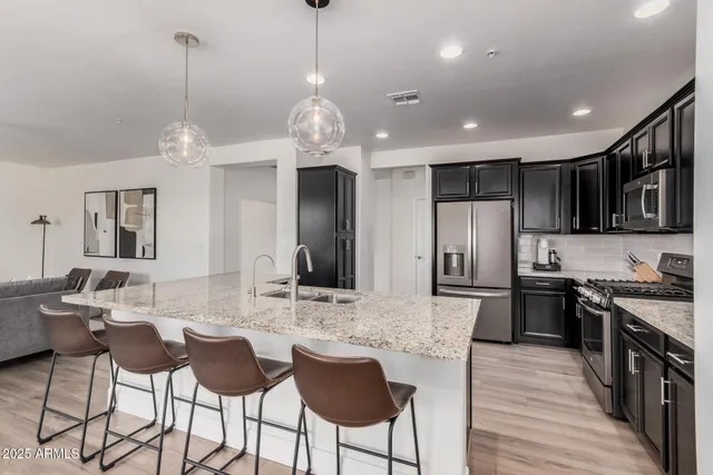 a kitchen with stainless steel appliances kitchen island granite countertop a dining table chairs refrigerator and cabinets