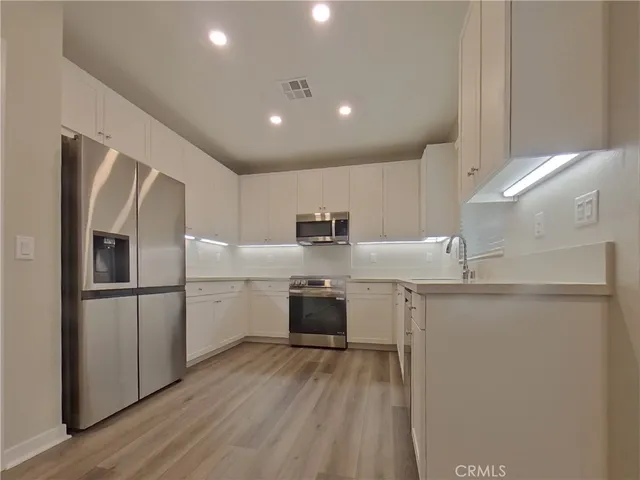 a kitchen with stainless steel appliances granite countertop a refrigerator a sink dishwasher a stove and white countertops with wooden floor