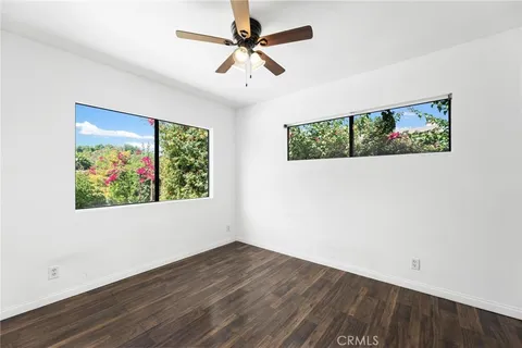 an empty room with wooden floor ceiling fan and windows