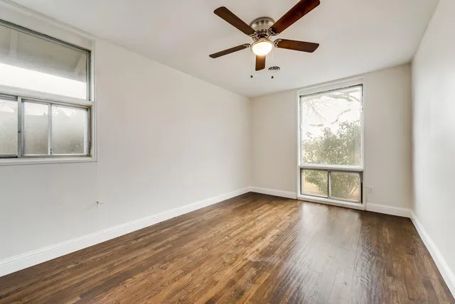 an empty room with wooden floor fan and windows