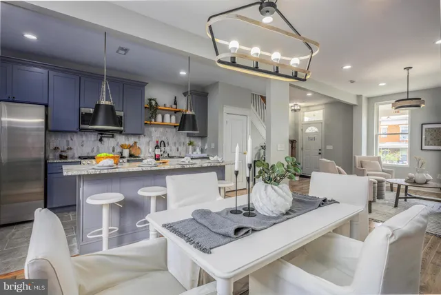 a kitchen with stainless steel appliances granite countertop a refrigerator a sink dishwasher a dining table and chairs with wooden floor