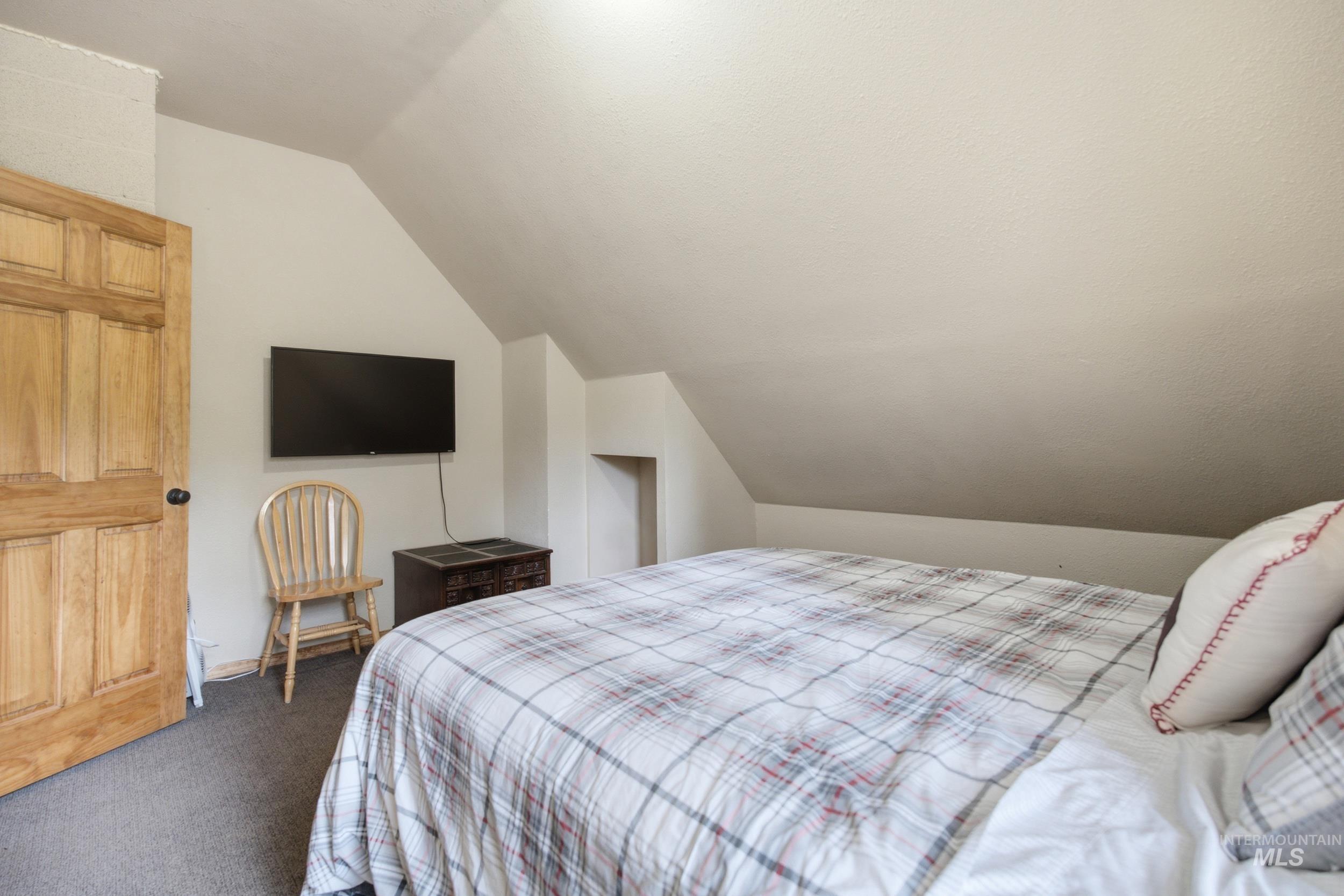 3980 North Pine-Featherville Road Mountain Home, ID 83647 - Photo 27 of 35 Carpeted room featuring a natural wood panel door, wall-mounted television, and sloped ceiling