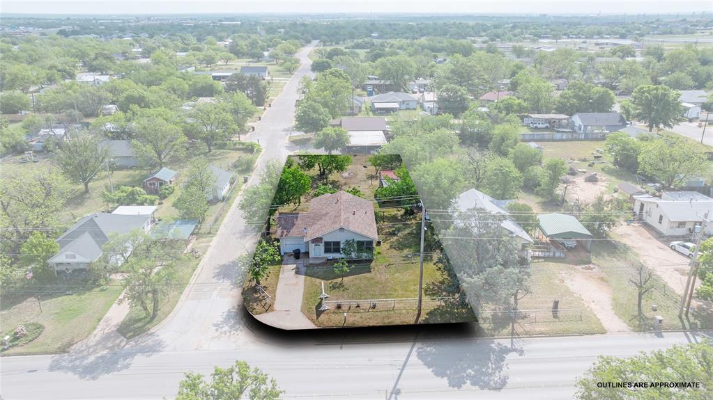 Aerial view of the property, featuring a single-story home with a brown roof and a driveway, set within a residential area with surrounding greenery