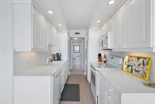 a kitchen that has a lot of white cabinets and stainless steel appliances