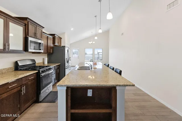 a kitchen with stainless steel appliances granite countertop a stove top oven a sink dishwasher a dining table and chairs with wooden floor