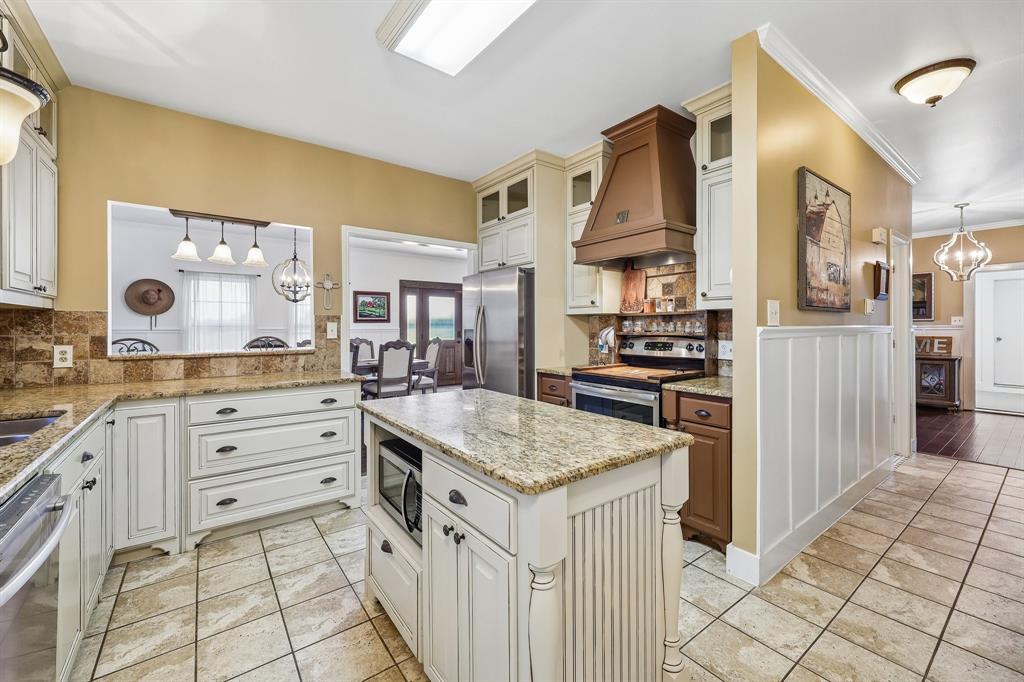 331 Radecke Road Krum, TX 76249 - Photo 19 of 40 Kitchen featuring a central island with built-in microwave, white cabinetry, granite countertops, and a tile backsplash