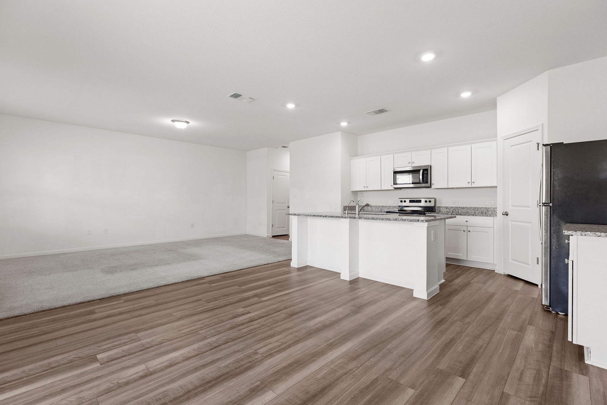 409 Line Of Fire Way Jarrell, TX 76537 - Photo 10 of 30 Open-concept living area featuring wood-finish flooring, kitchen island with stone countertops, white cabinetry, stainless steel appliances, recessed lighting, and adjoining dining space.