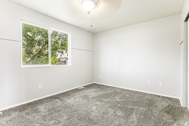 4239 West 5325th Street South Roy, UT 84067 - Photo 9 of 26 Bright room featuring a large window, light gray walls, plush gray carpeting, and a ceiling fan with integrated lighting