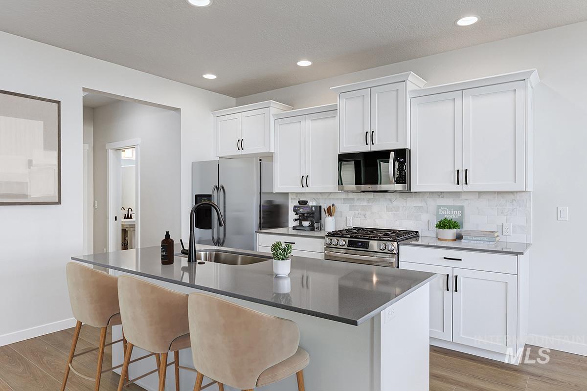 224 West Broyhill Street Meridian, ID 83642 - Photo 7 of 24 Kitchen featuring white cabinetry, stainless steel appliances, dark stone countertops, a kitchen bar, and a textured ceiling