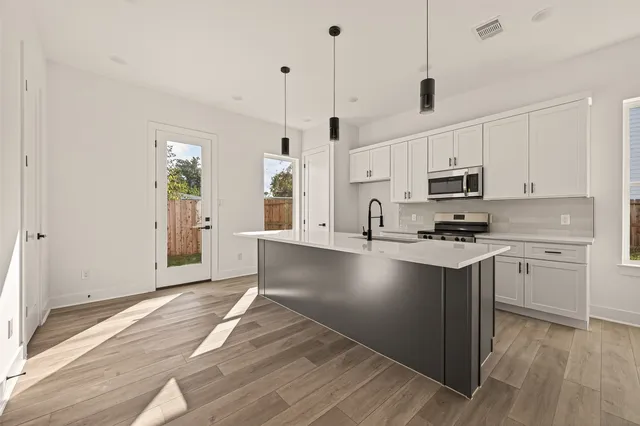 a open kitchen with stainless steel appliances granite countertop a stove a sink a refrigerator and white cabinets with wooden floor