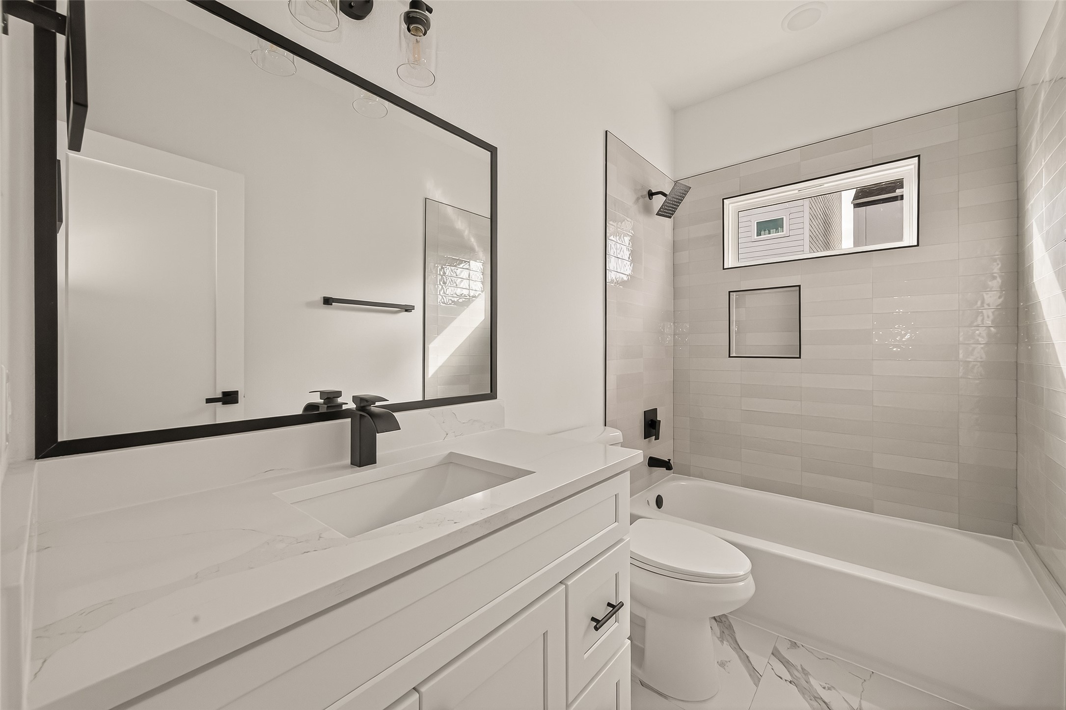 2475 Carmel Street, Unit B Houston, TX 77091 - Photo 15 of 21 Enjoy a naturally lit, contemporary secondary bath designed with black hardware, a framed mirror, and a calming neutral tile for a clean, elevated feel.