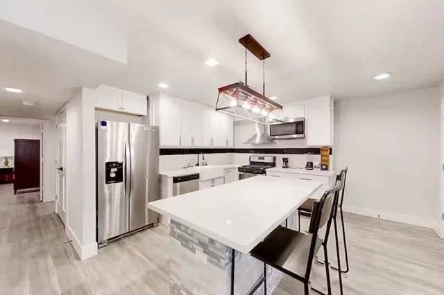 a kitchen with stainless steel appliances a refrigerator a sink dishwasher a stove and a dining table with wooden floor