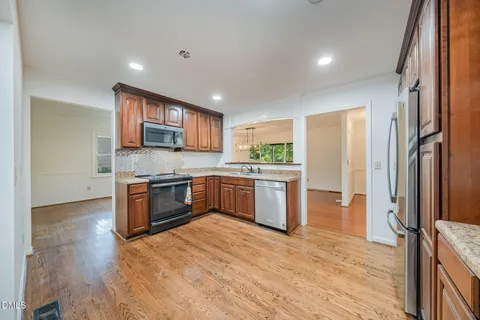 a large kitchen with stainless steel appliances granite countertop a stove a sink dishwasher and a refrigerator with wooden floor