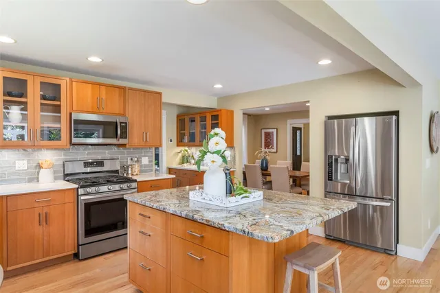 a kitchen with stainless steel appliances granite countertop a stove top oven a sink dishwasher a dining table and chairs with wooden floor