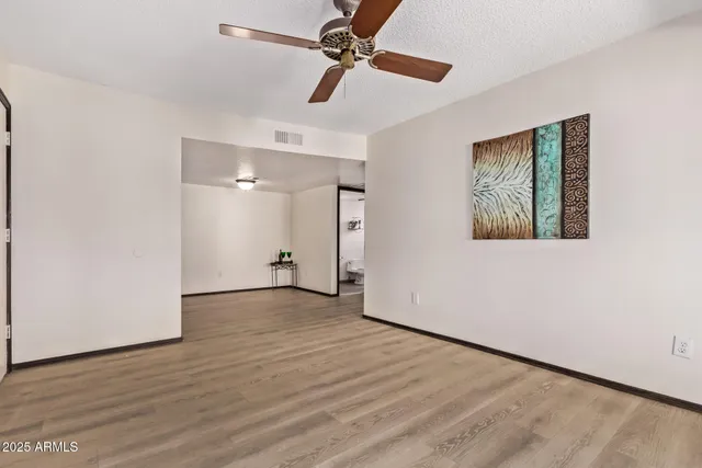 a view of an empty room with wooden floor and a ceiling fan