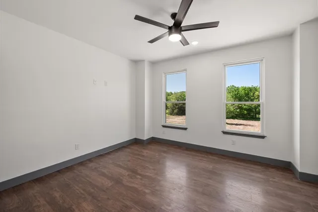 an empty room with wooden floor ceiling fan and windows