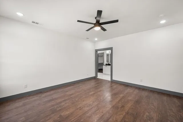 a view of an empty room with wooden floor and a ceiling fan