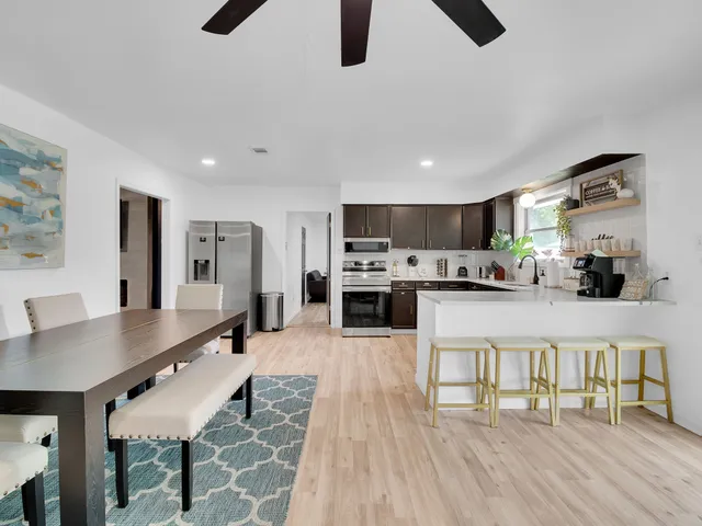 a kitchen with stainless steel appliances granite countertop a stove top oven a sink a dining table and chairs with wooden floor