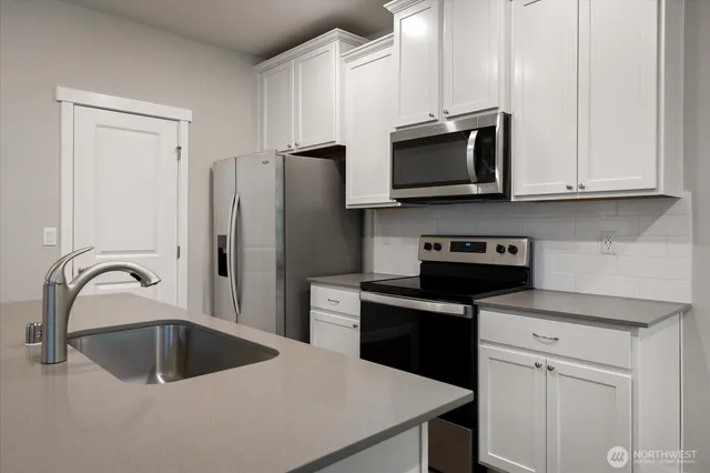 a kitchen with stainless steel appliances granite countertop a sink a stove and a refrigerator with white cabinets