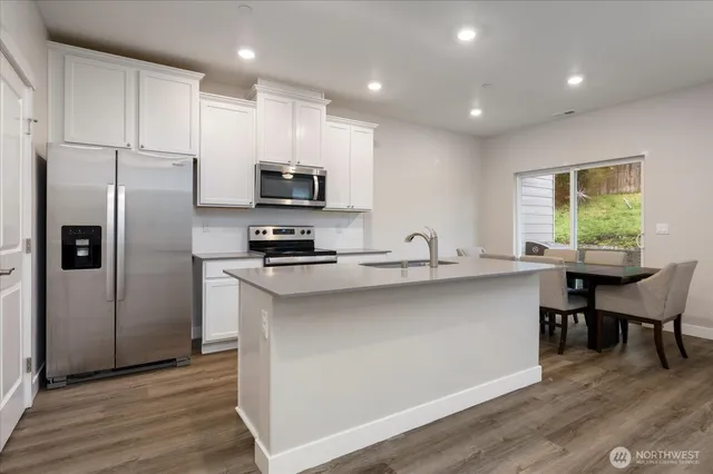 a kitchen with stainless steel appliances a refrigerator a stove a sink a dining table and chairs with wooden floor