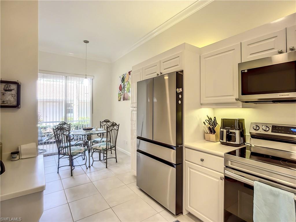 14530 Red Fox Run, Unit 215 Naples, FL 34110 - Photo 5 of 28 a kitchen with stainless steel appliances granite countertop a refrigerator a stove a dining table and chairs with wooden floor