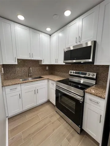 a kitchen with granite countertop a stove a microwave a sink and cabinets