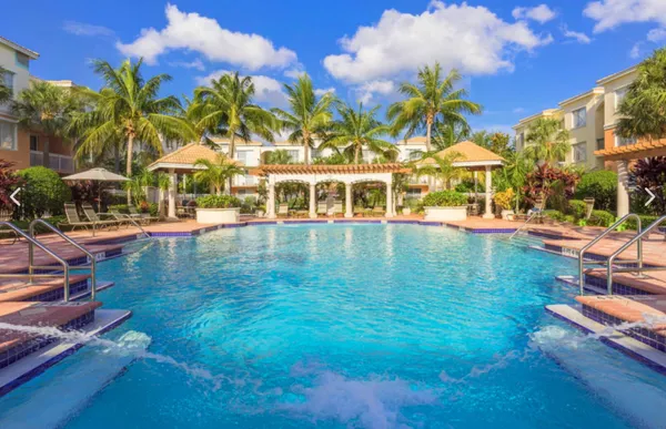 a view of a swimming pool with a lawn chairs under an umbrella with palm trees