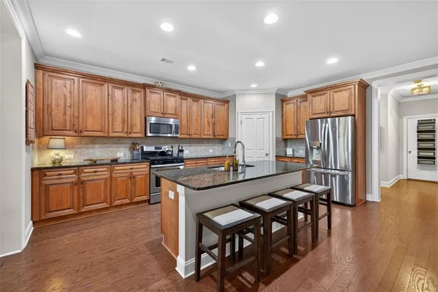 a kitchen with stainless steel appliances granite countertop wooden cabinets a refrigerator a stove a sink and a island with wooden floor