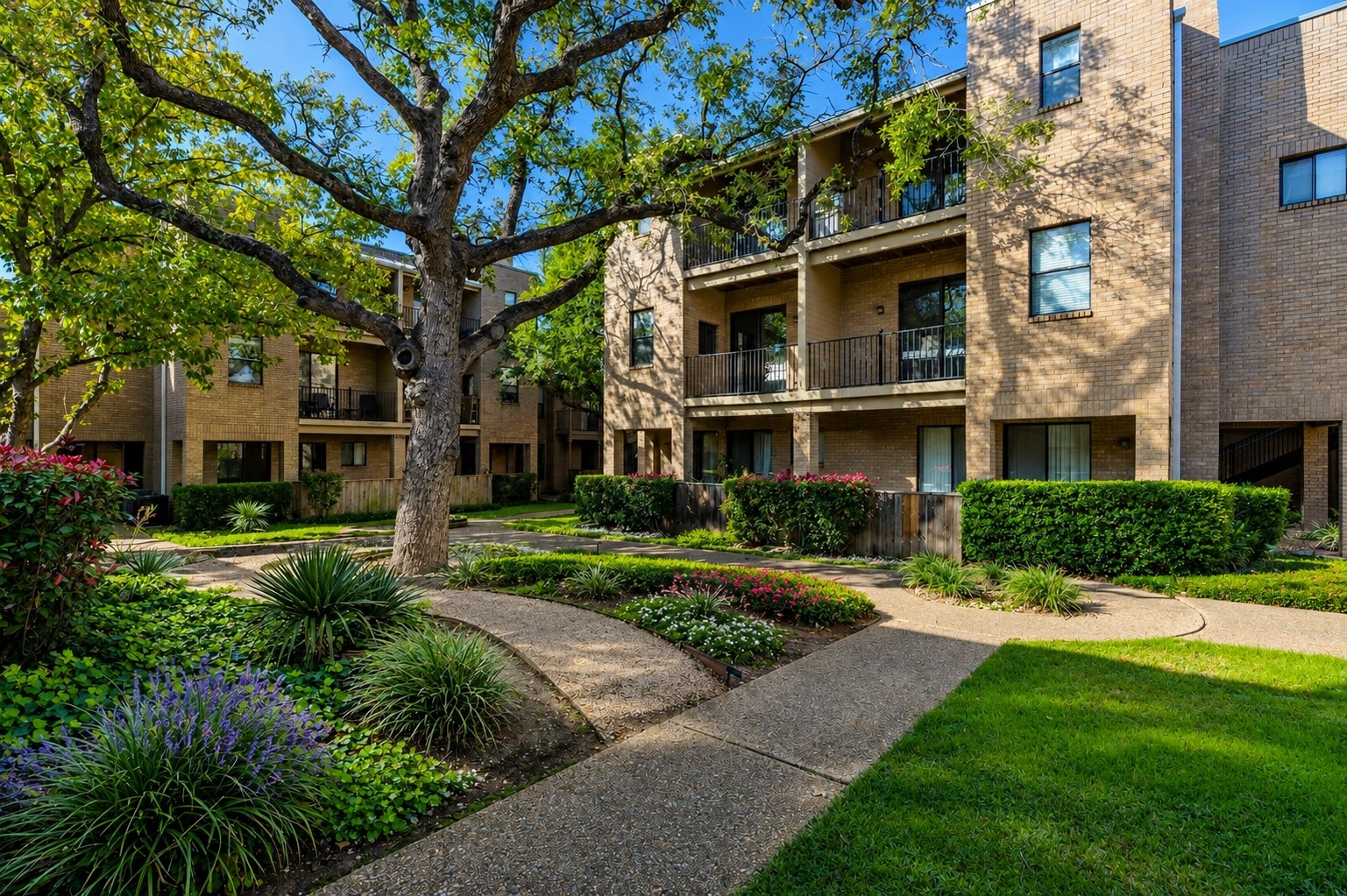 611 East 45th Street, Unit 25 Austin, TX 78751 - Photo 1 of 21 Exterior brick building featuring multiple levels with balconies, mature trees, manicured lawns, and winding pathways