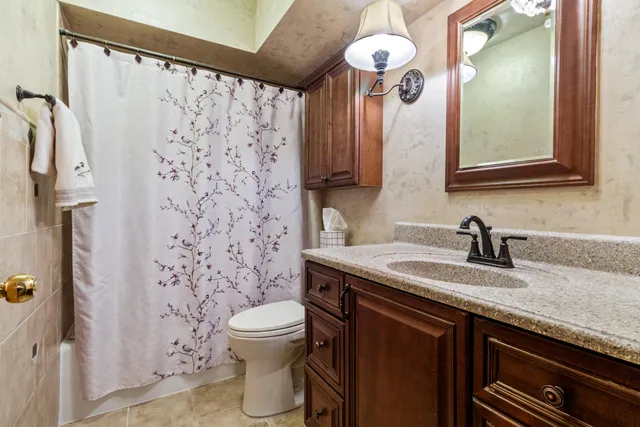 a bathroom with a granite countertop sink a toilet a mirror and shower curtain