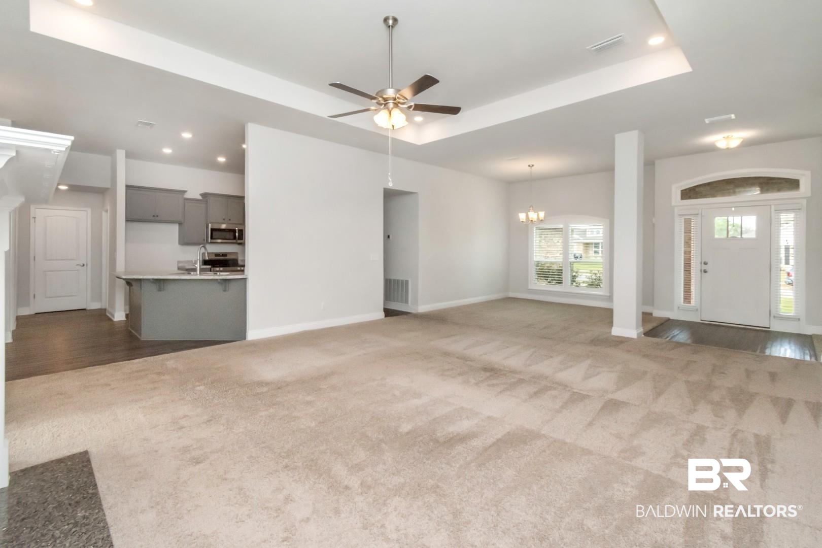 6632 Monarch Circle Mobile, AL 36618 - Photo 6 of 32 Unfurnished living room featuring a tray ceiling, a ceiling fan, dark carpet, and suspended lighting
