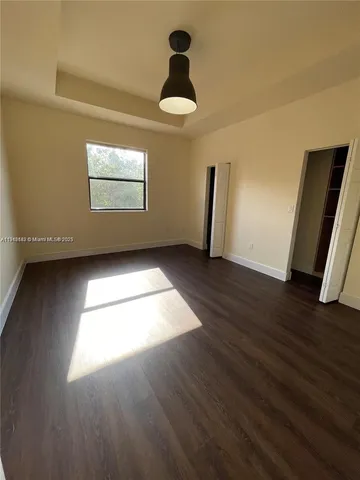 an empty room with wooden floor chandelier fan and windows