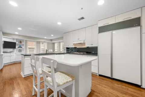 a kitchen with stainless steel appliances granite countertop a refrigerator a stove a sink a dining table and chairs with wooden floor