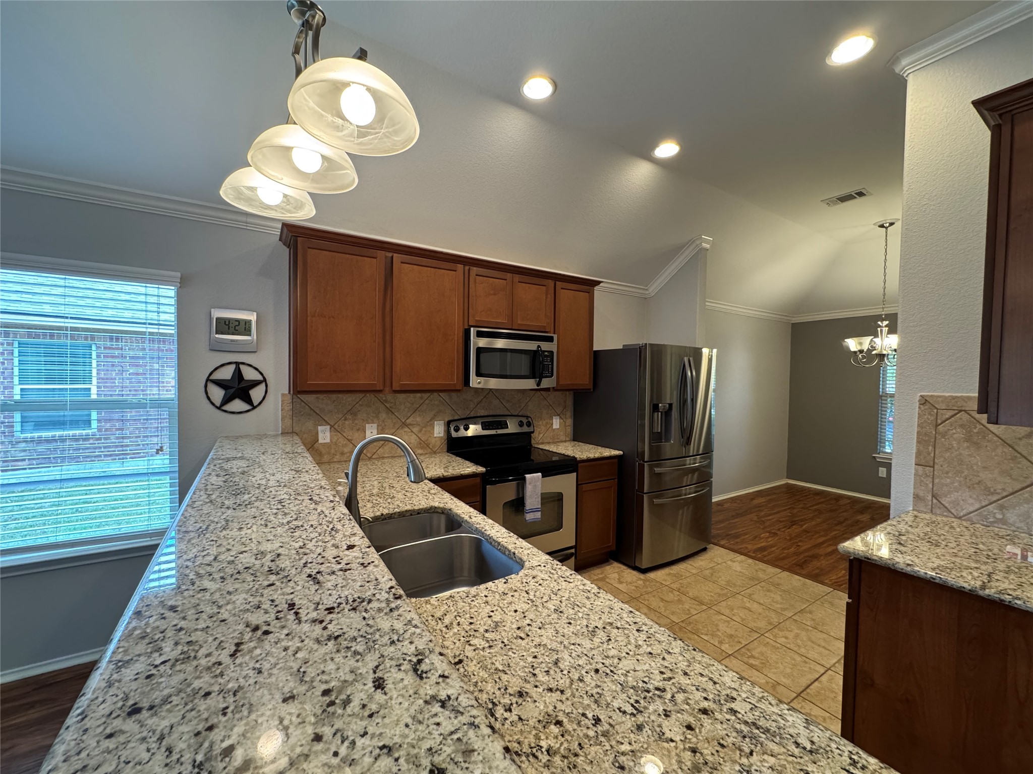 112 Eagle Owl Loop Leander, TX 78641 - Photo 5 of 17 Kitchen featuring crown molding, lofted ceiling, hanging lights, stainless steel appliances, and light stone counters