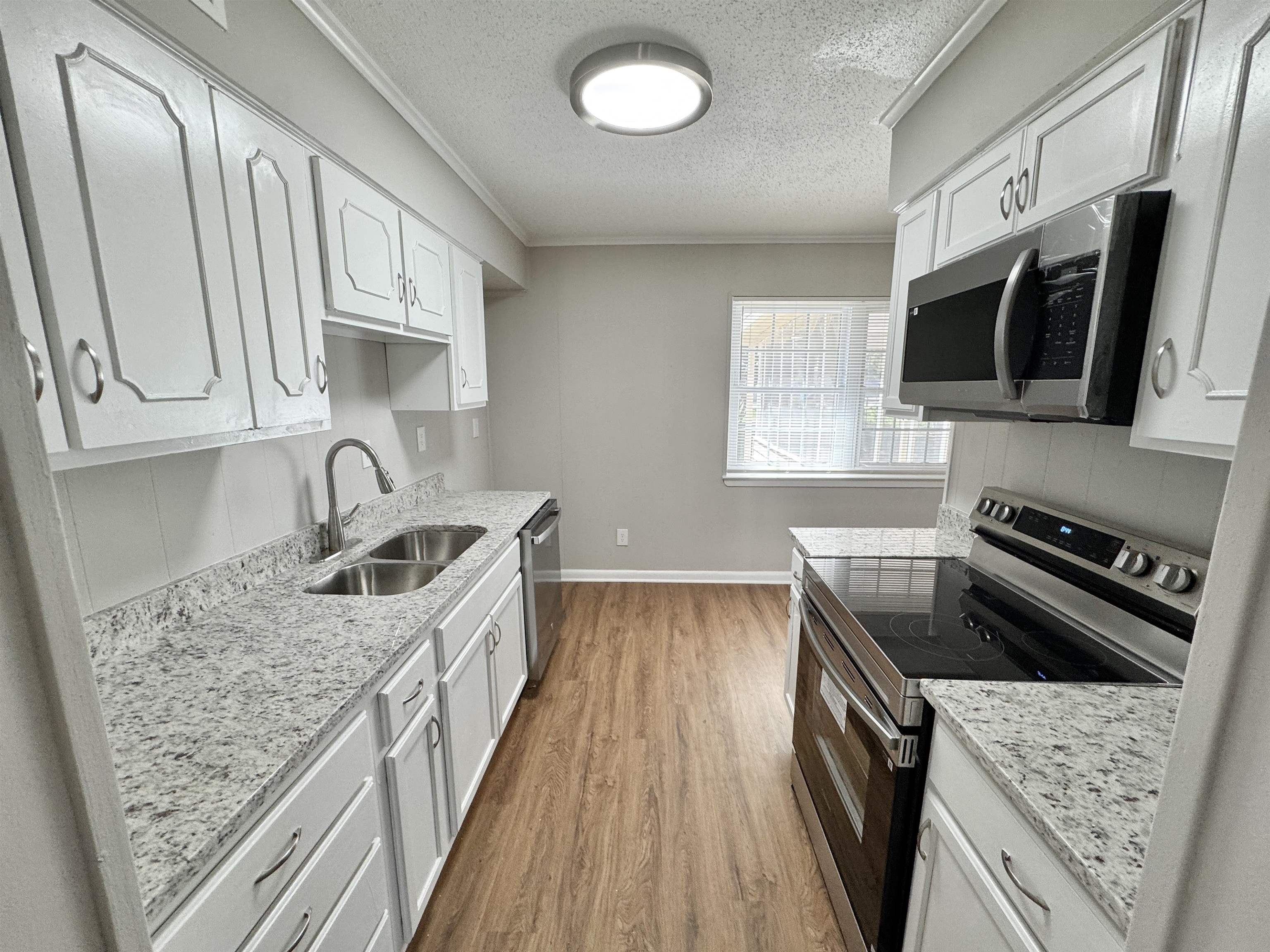 5095 Bowie Road Memphis, TN 38109 - Photo 5 of 25 Kitchen featuring stainless steel appliances, a textured ceiling, wood finished floors, ornamental molding, and light stone counters