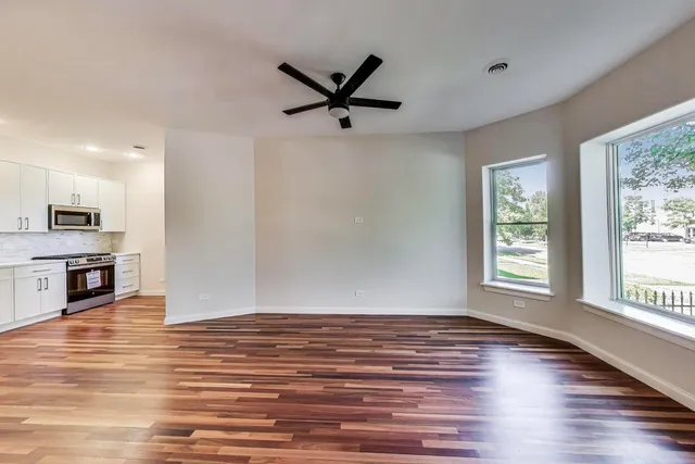 a view of a livingroom with wooden floor a ceiling fan and windows