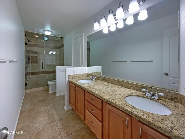 a bathroom with a granite countertop double vanity sink and mirror with shower