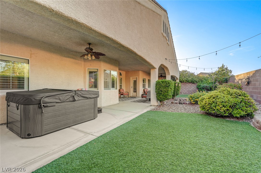1604 Cattle Ranch Place Henderson, NV 89002 - Photo 74 of 99 Relax in the private spa nestled under a covered patio, overlooking a vibrant green yard with string lights for evening ambiance.