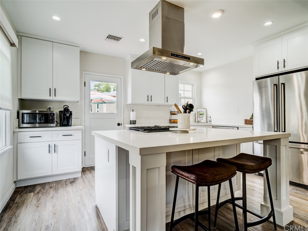 3758 Chatwin Avenue Long Beach, CA 90808 - Photo 11 of 34 a kitchen with stainless steel appliances a sink a stove a refrigerator and white cabinets with wooden floor