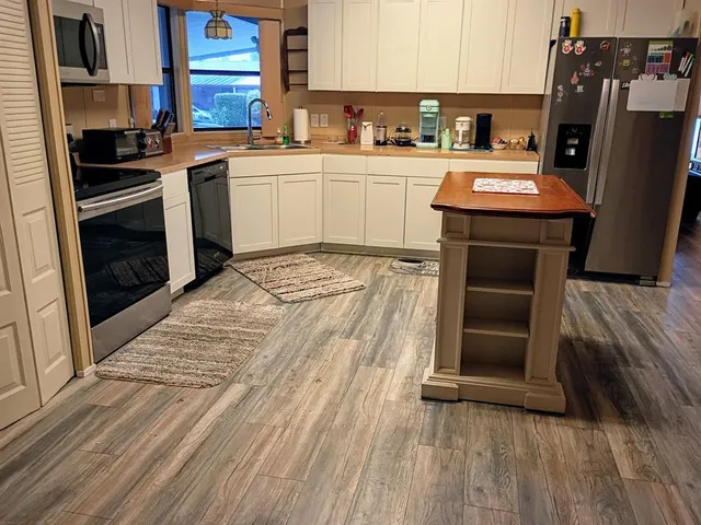 a kitchen with stainless steel appliances granite countertop a refrigerator a sink dishwasher a stove and white countertops with wooden floor