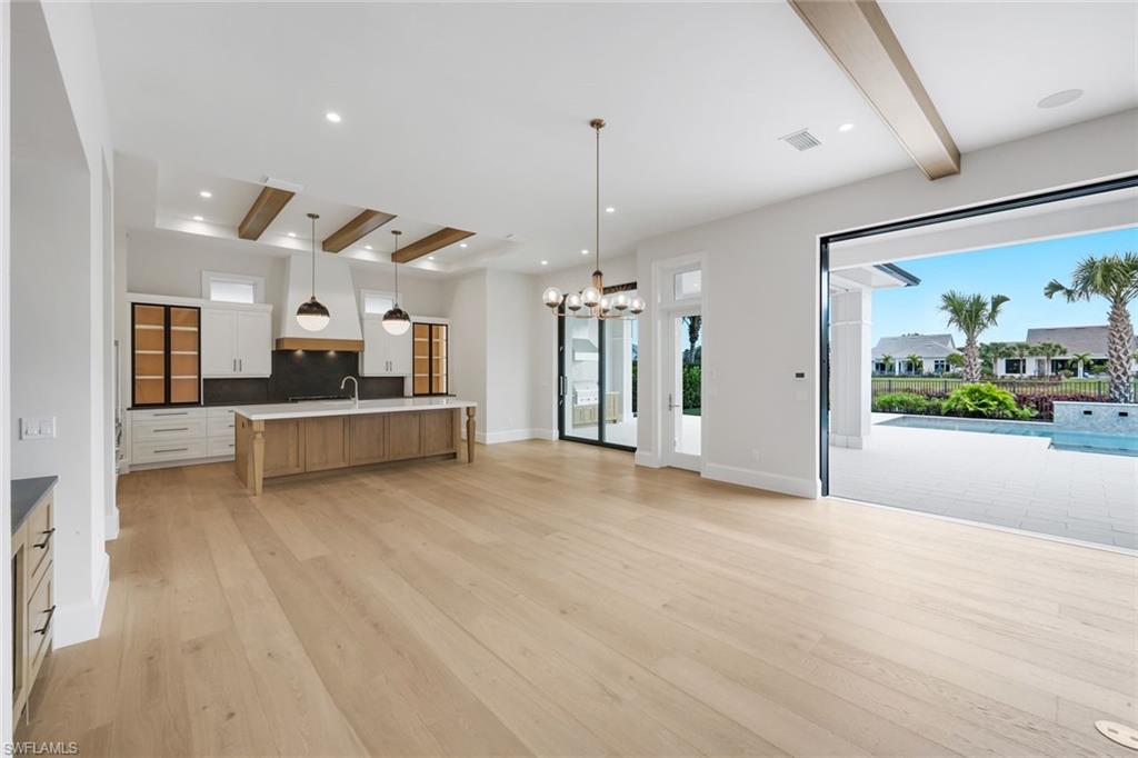 16728 Enclave Circle Naples, FL 34110 - Photo 49 of 49 Kitchen featuring beam ceiling, two tone cabinetry, a large island with sink, open floor plan, and light wood finished floors