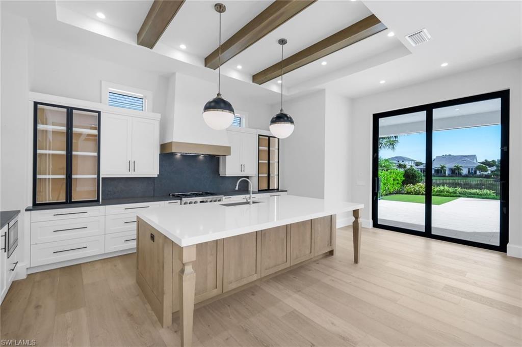 16728 Enclave Circle Naples, FL 34110 - Photo 12 of 49 Two tone kitchen featuring beam ceiling, dual tone cabinetry, decorative light fixtures, a spacious island, and tasteful backsplash
