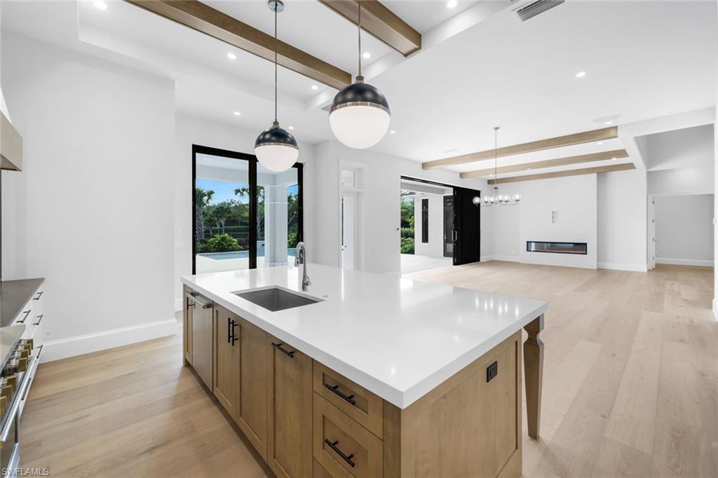 16728 Enclave Circle Naples, FL 34110 - Photo 13 of 49 Kitchen with beam ceiling, light wood-type flooring, a kitchen island with sink, stainless steel range, and light stone counters