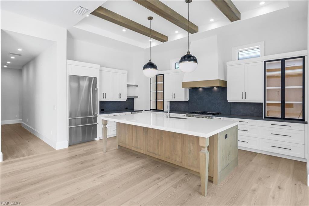 16728 Enclave Circle Naples, FL 34110 - Photo 16 of 49 Two tone kitchen featuring two tone color scheme, high quality fridge, pendant lighting, decorative backsplash, and a large island with sink